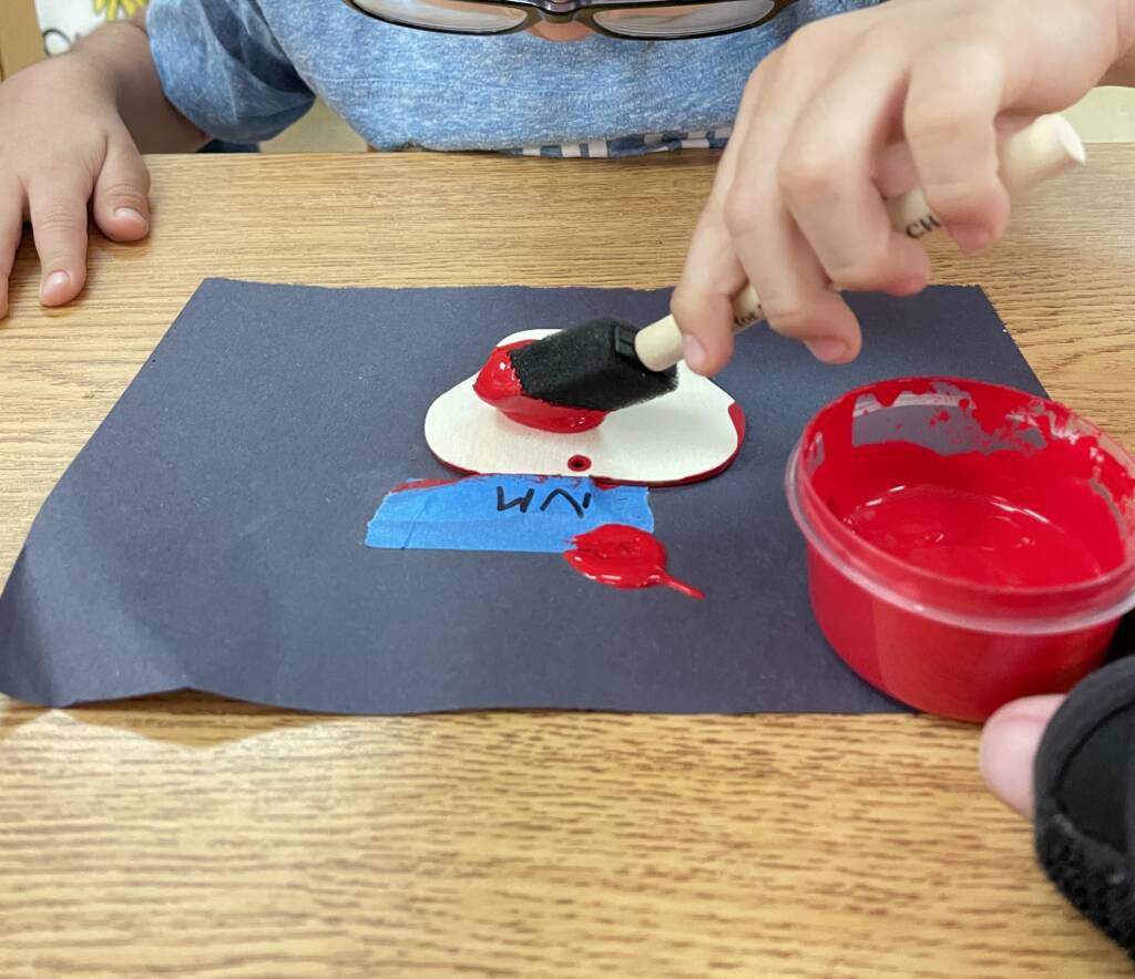 Student painting a wooden apple red.