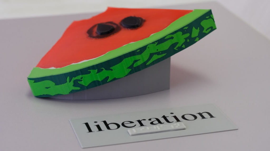 A tactile watermelon art piece and the word "liberation" in both braille and print