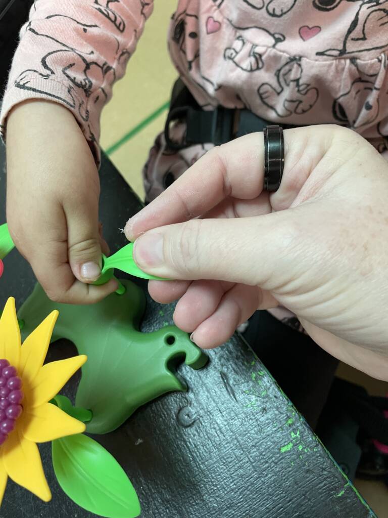 Student putting the pieces of the plastic flowers together with a teacher.