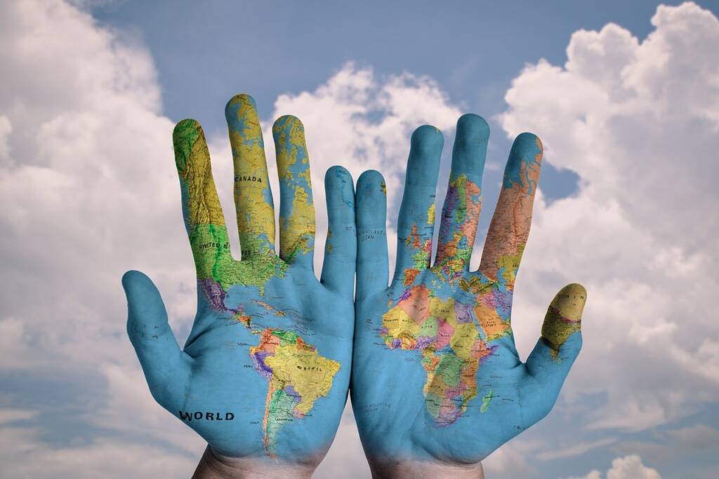 A pair of hands with a globe painted on them with all the countries and oceans.
A sky with clouds is behind the hands.