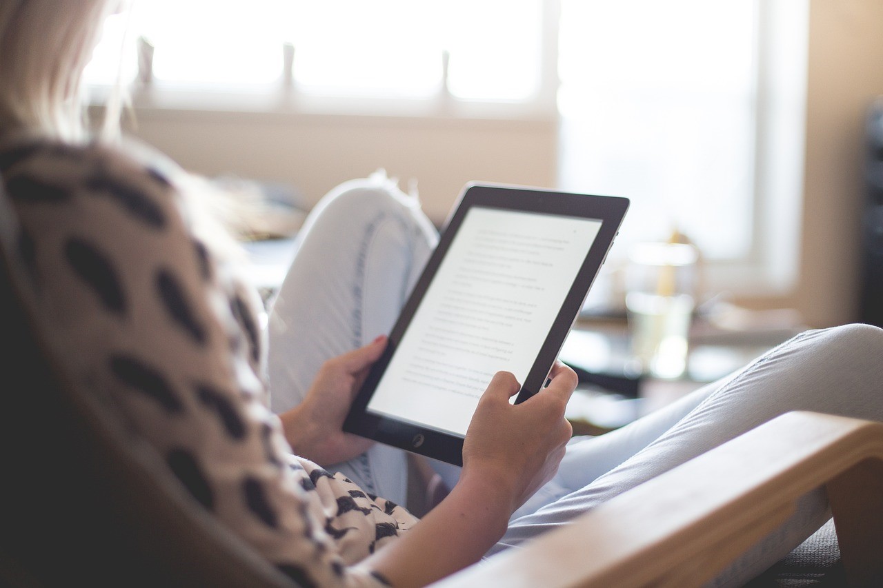 Woman relaxing on a chair reading on her electronic device.