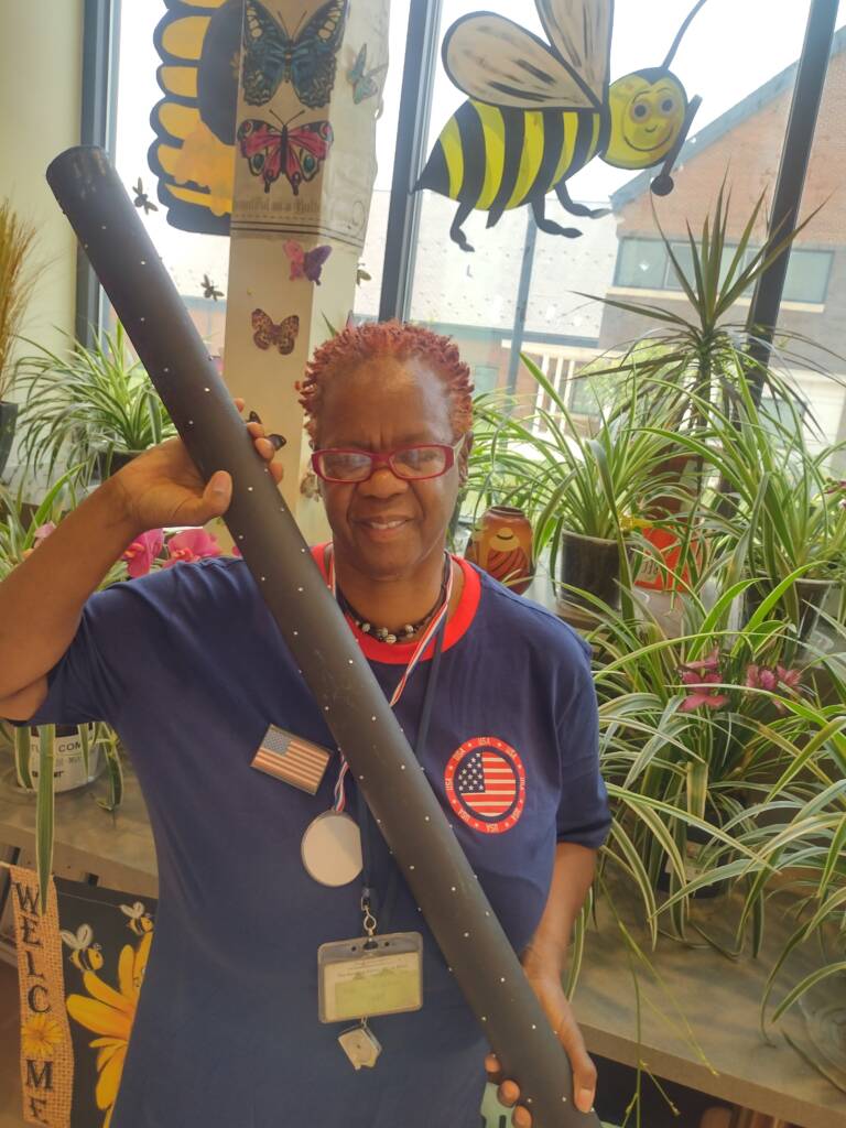 Gwen holding the rainstick in front of her classroom plants.