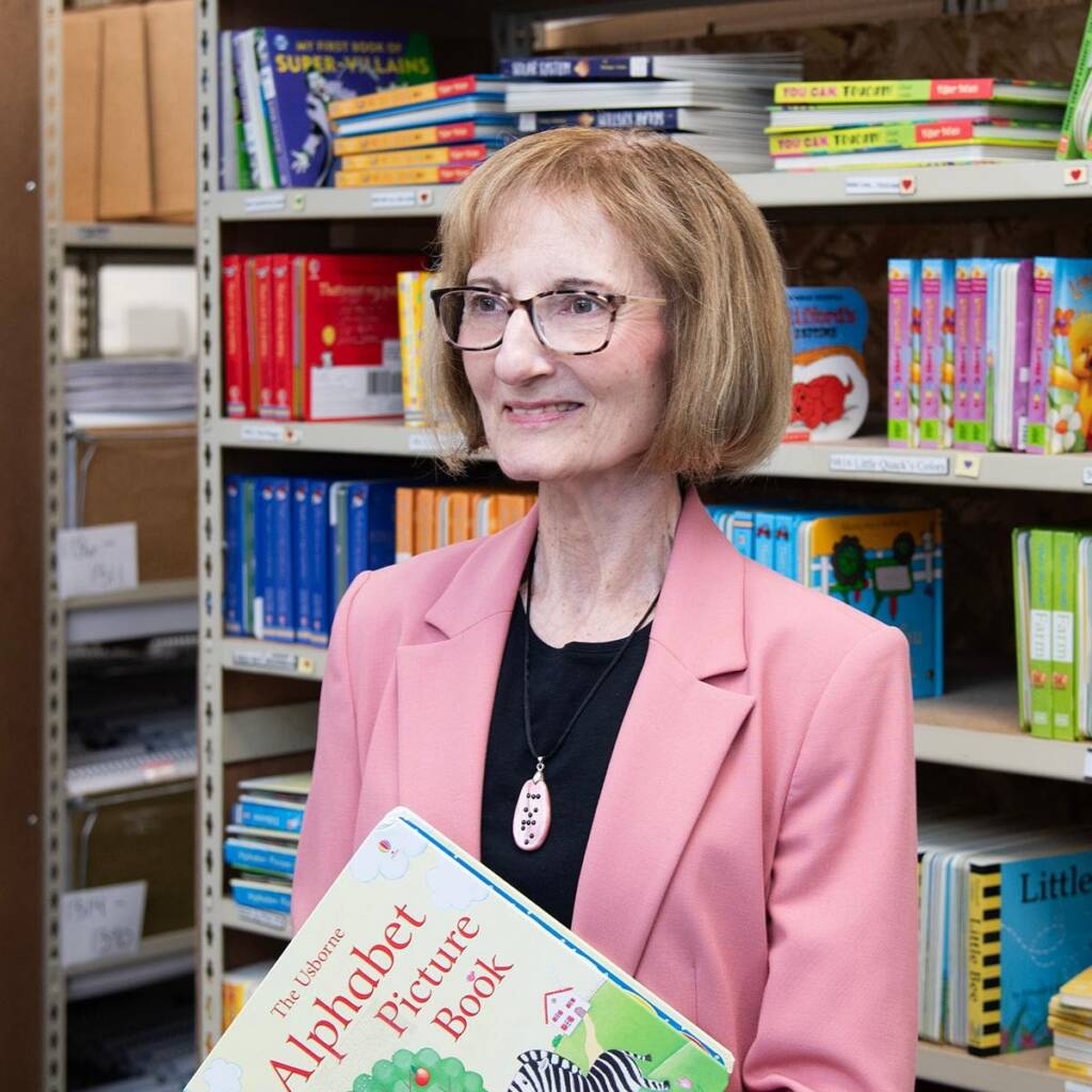 Photo of Debra holding a book in front of a bookshelf.