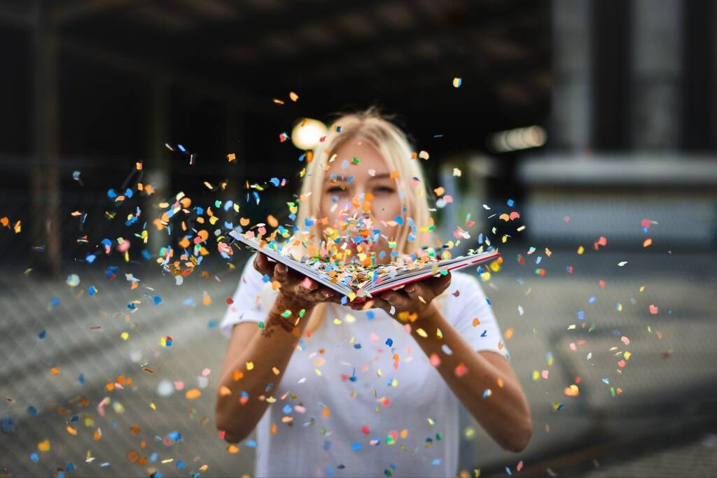 woman blowing confetti off of a book