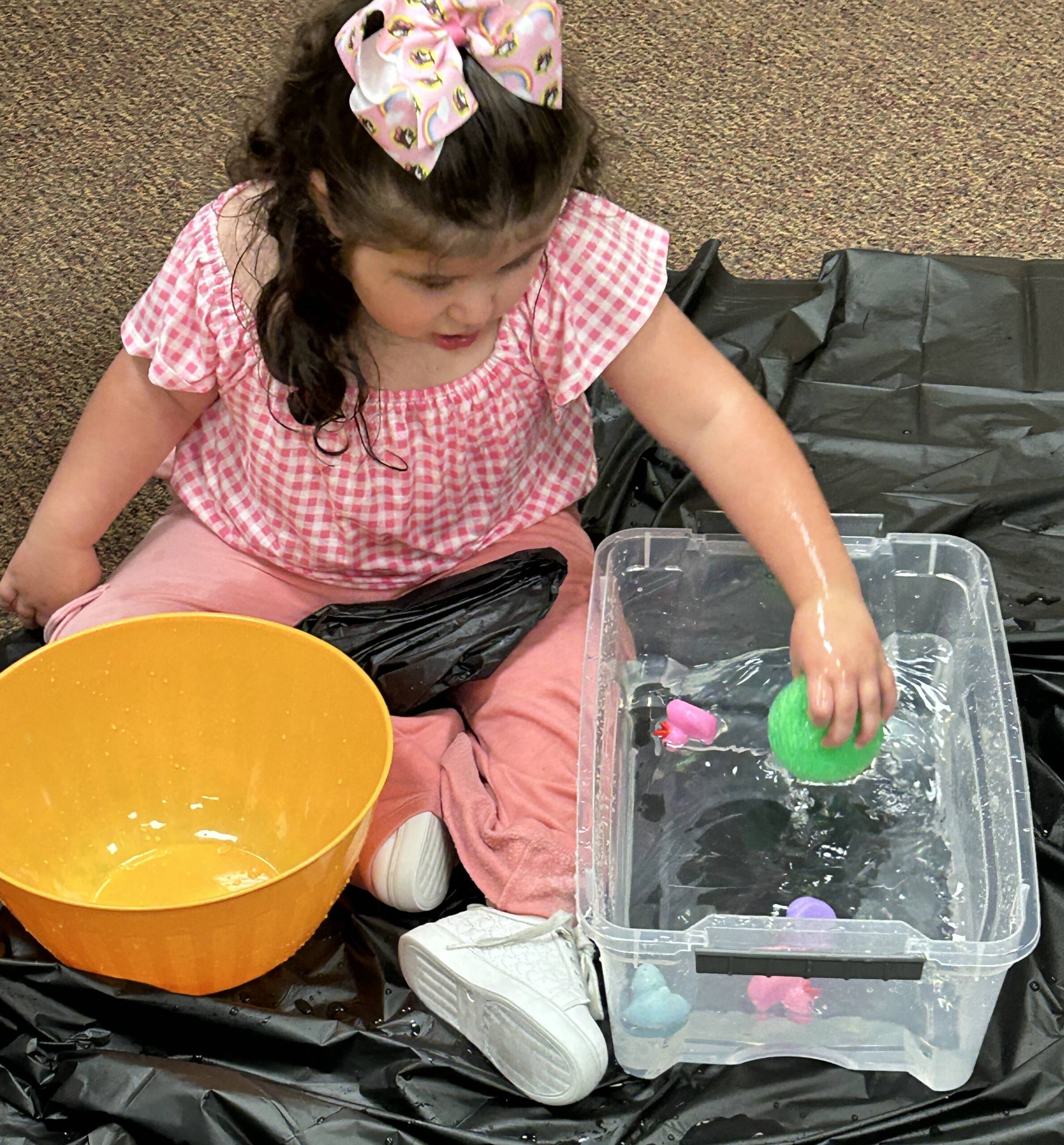 Young girl sitting on the floor with doing a water play activity.