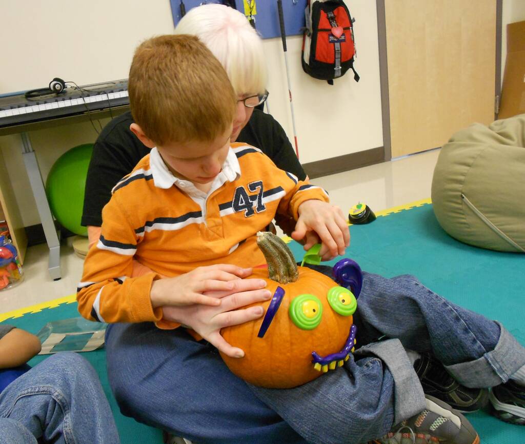 Kathi with a student on her lap exploring a small jack-o-lantern using hand under hand technique.