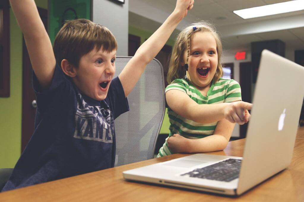 A boy and girl excited and cheering while looking at the screen of a laptop.