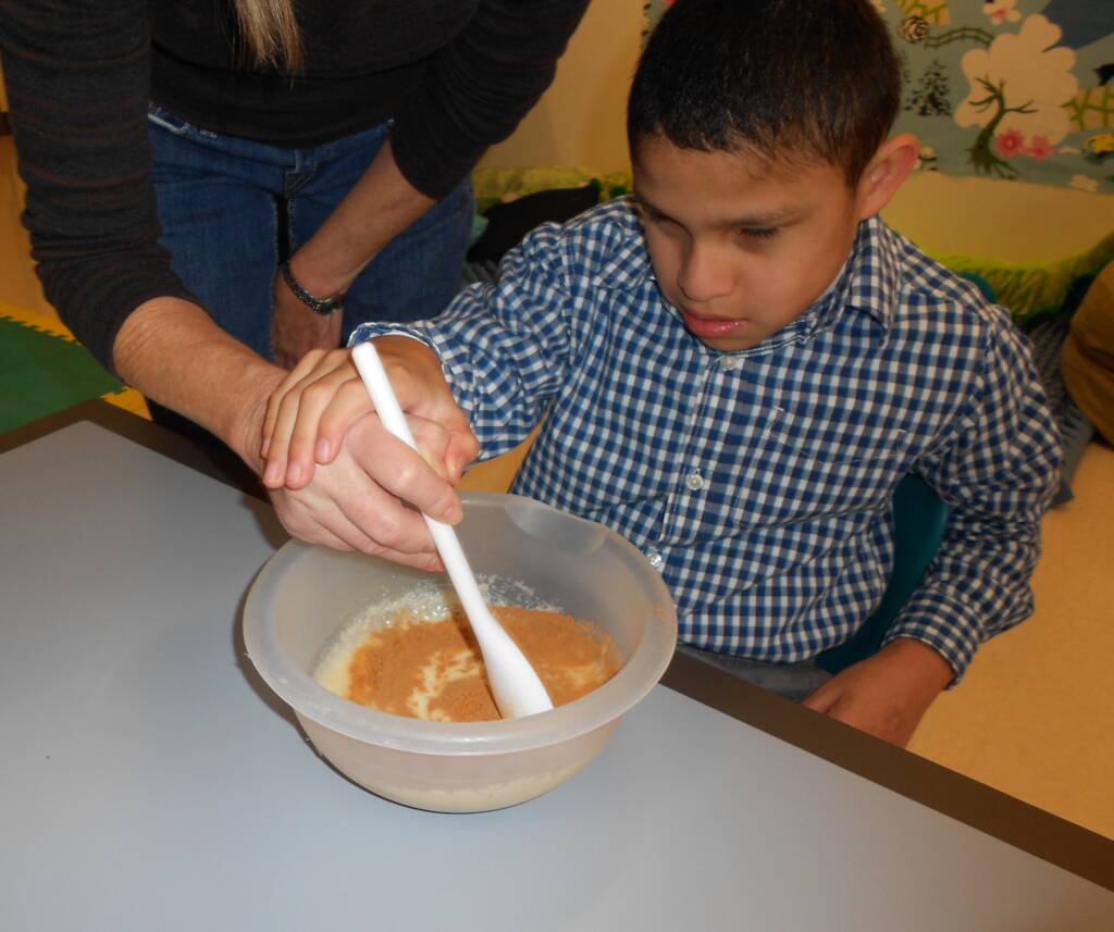 Student mixing ingredients with hand under hand with teacher.