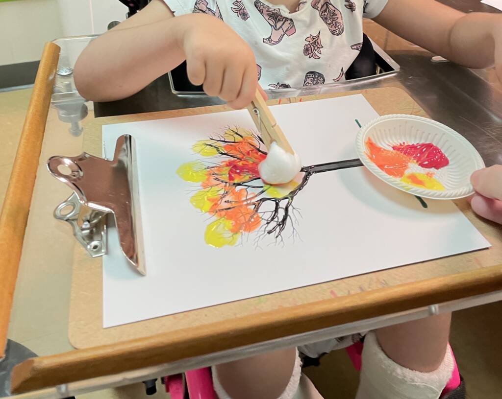 Student painting a tree with a clothespin and a cotton ball.